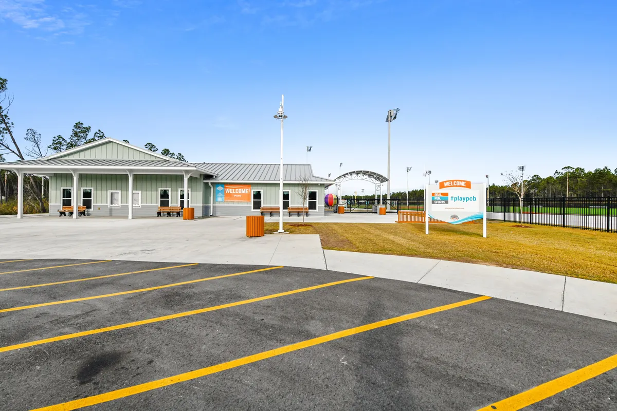 A welcoming exterior shot featuring a prominent community welcome sign, the main building, and a playground area nearby. The setting is lively, with families gathering and children playing, emphasizing a communal atmosphere.