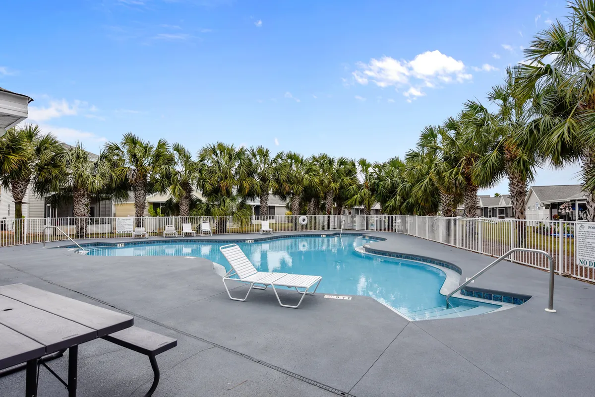 A well-maintained swimming pool area bordered with palm trees and lounge chairs, radiating a laid-back resort ambiance. The setting sun hints at relaxing evenings by the water, while the space is designed for both activity and leisure.