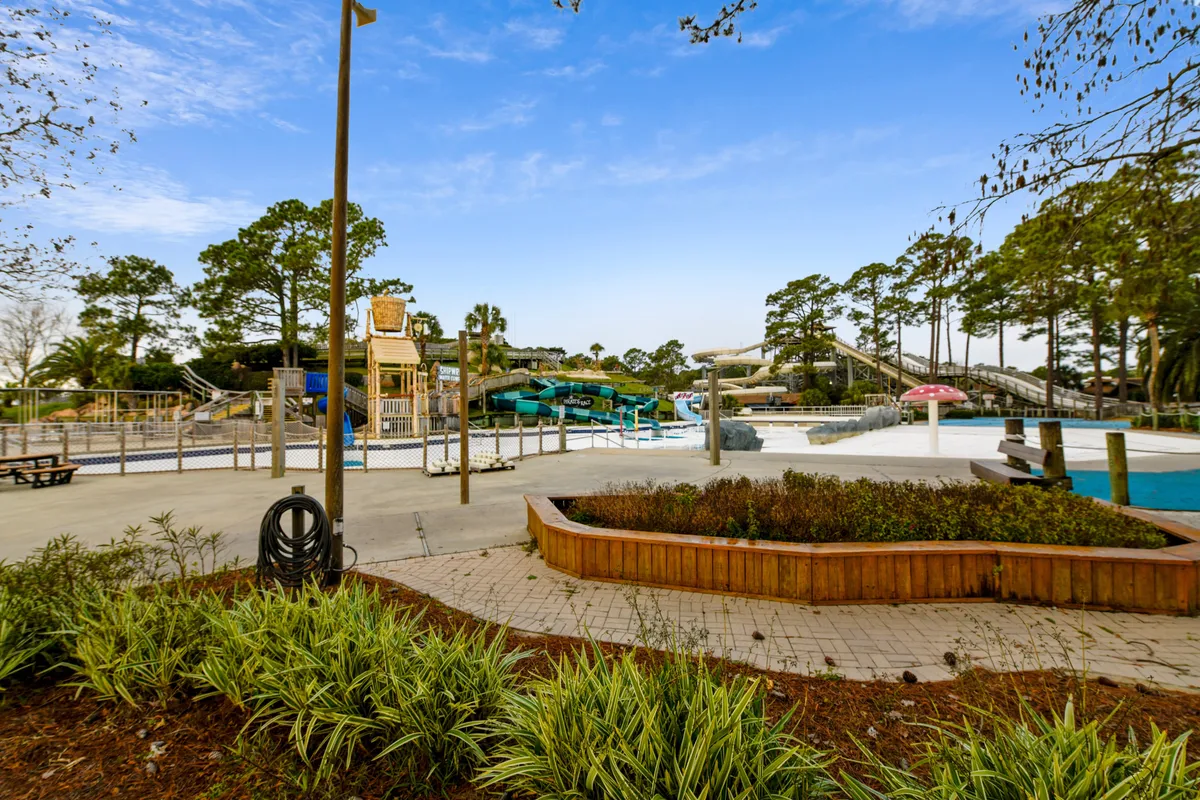 A vibrant outdoor pool area with water slides, play structures, and lush greenery. The scene is filled with joyful energy, reflecting summer fun, memorable afternoons, and poolside gatherings for all ages.