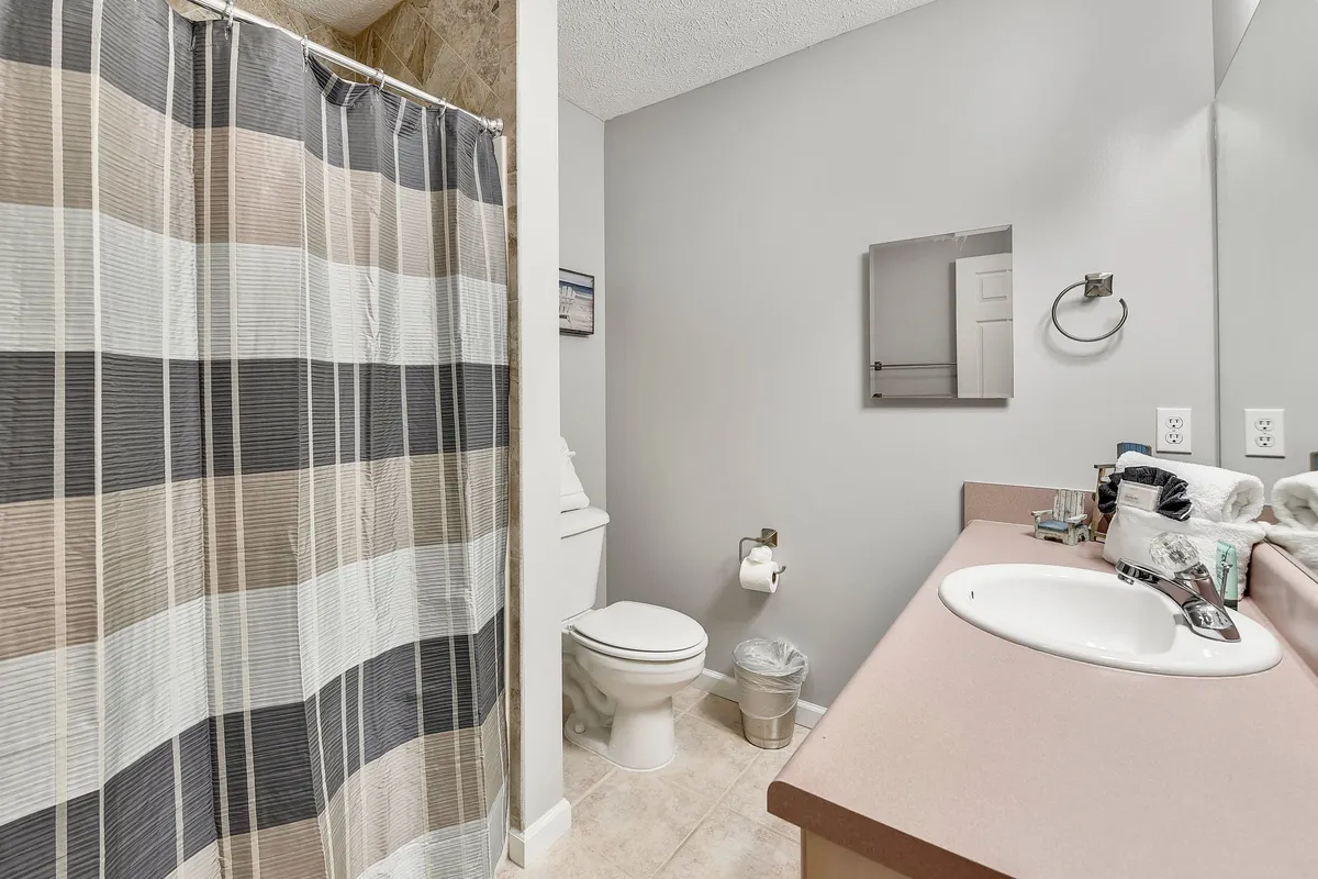 A bright, practical bathroom featuring a striped shower curtain, vanity with sink, and toilet. The space feels clean and functional, ideal for quick morning routines or relaxing after the beach.