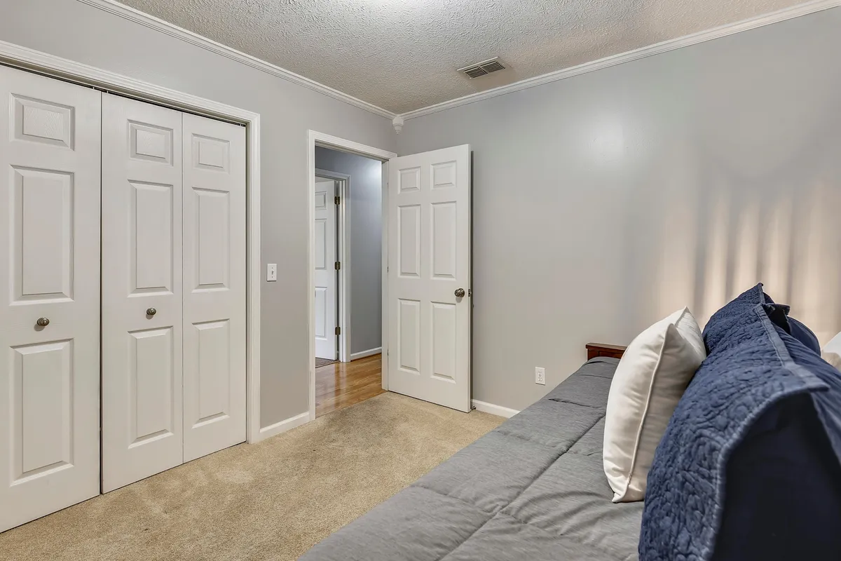 A twin size day bed with a trundle, bi-fold closet doors, and an open door to the hallway. The room is calm and cozy, ideal for children or friends, and offers a peaceful space for rest or late-night fun.
