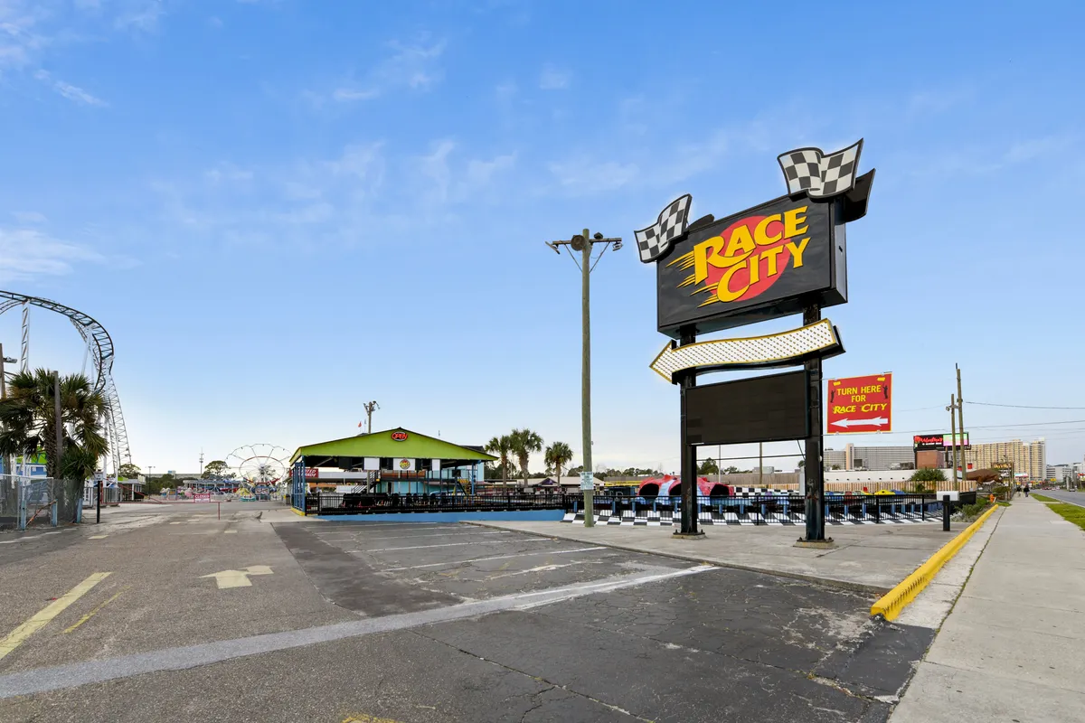 This energetic image captures the Race City amusement park entrance, with a lively go-kart track, roller coaster in the background, and a checkered Race City sign. Covered seating and dining areas are visible, enhancing the sense of family adventure and local attractions nearby.